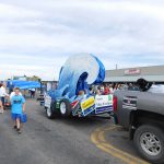 Parade marchers and float with blue wave on trailer