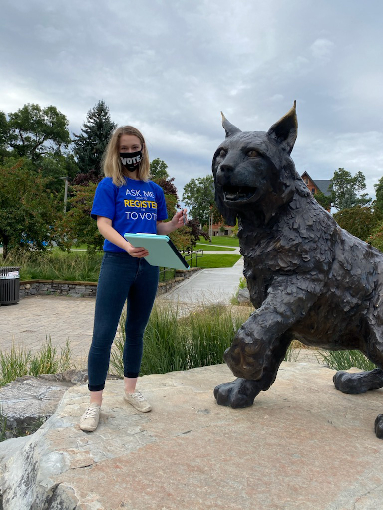 A person with a clipboard ready to register voters standing next to a bobcat statue.